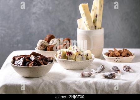 Auswahl an hausgemachten Schokoladen-Mandelnüssen aus Toffee, dunkler Schokolade-Trüffel, weißer Schokolade-Süßigkeitenbar in Schüsseln auf weißem Leinentischtuch. Handmad Stockfoto