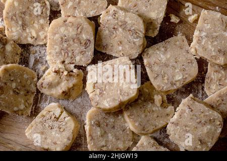 Hausgemachter Shortbread-Teig zum Kochen von Zuckerkeksen mit Nüssen und weißer Schokolade auf Holzschneidebrett schneiden. Hausgemachen süßes Backen. Draufsicht, close- Stockfoto
