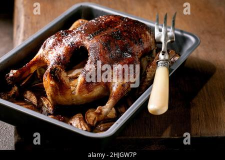 Klassisches Urlaubsgericht geröstete glasierte Ente mit Äpfeln im Backblech mit Fleischgabel über Holztisch. Stockfoto