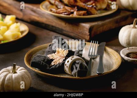 Festtagstisch mit klassischen Gerichten geröstete glasierte Ente mit Äpfeln, gekochten Kartoffeln und Sauce, leerer Keramikplatte mit Serviette und Herbstblatt Stockfoto