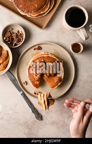 Hände, die einen Stapel Pekannüsse aus Ahornholz mit karamellisierten Bananen auf einem Teller bauen. Stockfoto