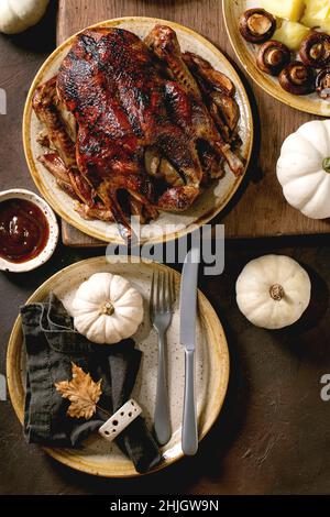 Tisch mit klassischen Gerichten geröstete glasierte Ente mit Äpfeln, gekochten Kartoffeln und Sauce, leerer Keramikplatte mit Serviette und Herbstblatt im Dunkeln Stockfoto