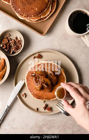 Hände, die einen Stapel Pekannüsse aus Ahornholz mit karamellisierten Bananen auf einem Teller bauen. Stockfoto