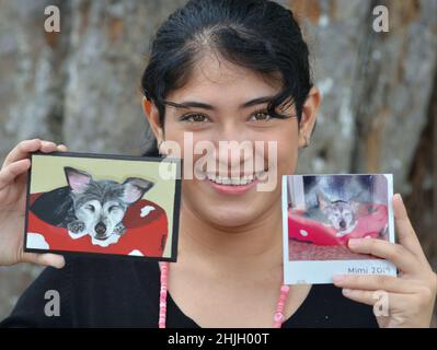 Lächelnd hübsche junge Tiermalerin mit schönen braunen Augen zeigt ein Foto und ihr maßgefertigtes Gemälde eines schlafenden Haustierhundes. Stockfoto