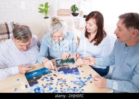 Familie spielen in Puzzles zu Hause, ältere Paare und Paare mittleren Alters arbeiten zusammen an einem Puzzle zu Hause Stockfoto