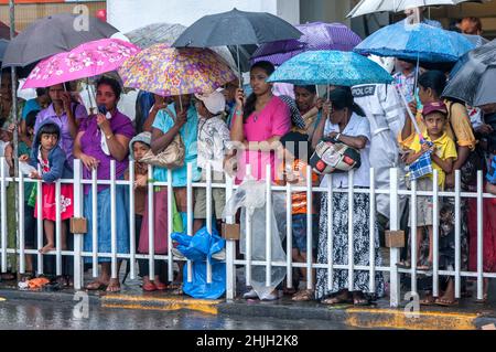 Eine Menge Menschen schützen sich unter Regenschirmen vor dem Regen, als sie auf den Start des Tages Perahera auf Sri Dalada Veediya in Kandy in Sri Lanka warten. Stockfoto