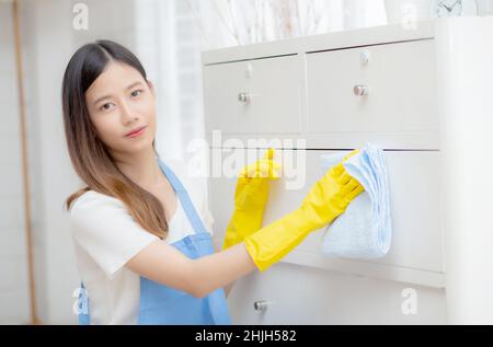 Junge asiatische Frau in Handschuhen Reinigung Haus im Zimmer, Haushälterin ist mit Stoff wischen, Hausmädchen und Service, Arbeiter polieren Staub im Wohnzimmer im Haus, Stockfoto