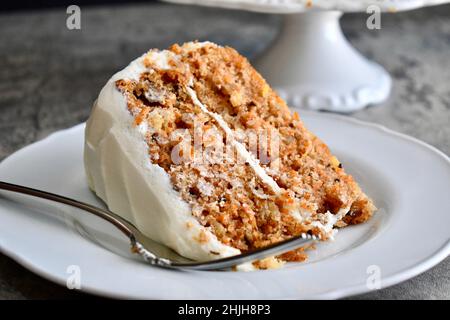 Ein Stück Karottenkuchen mit Frischkäse-Zuckerguss auf einem weißen Teller mit Gabel Stockfoto