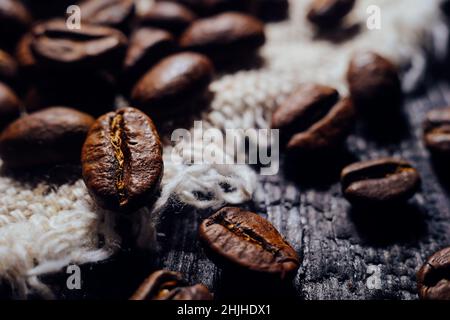Die Makrofotografie von Kaffeebohnen liegt auf strukturiertem Holz und Quappen. Frischer aromatischer Kaffee aus der Ernte. Selektive Fokussierung. Zurück zum Cafe, Restaurant oder Coffee Shop. Stockfoto