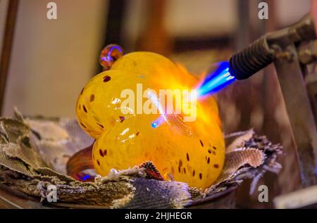 Glasgebläse formt eine Blase aus geschmolzenem Glas mit einem Blasbrenner im Herstellungsprozess in der Werkstatt eines Glasherstellers, geringe Schärfentiefe Stockfoto