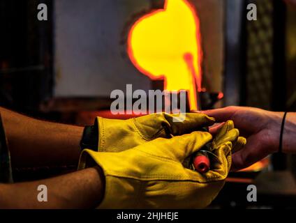 Glasgebläse, die eine Blase aus geschmolzenem Glas auf einem Stab im Ofen formt, Herstellungsverfahren in der Werkstatt eines Glasherstellers, geringe Schärfentiefe Stockfoto