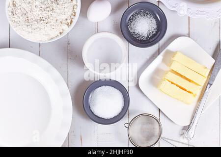 Zutaten aus Kuchenkruste in Schüsseln. Mehl, Zucker, Salz, Eiswasser, Butter und Ei auf Holztisch Stockfoto