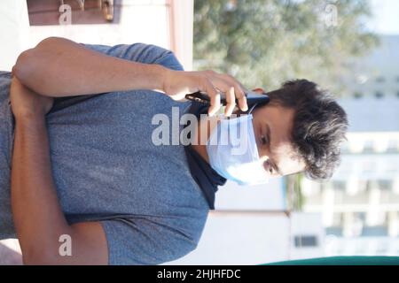 Porträt eines südasiatischen Mannes, der eine medizinische Maske trägt und im Freien auf dem Mobiltelefon spricht Stockfoto