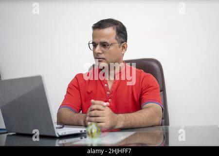 Indischer Mann in Brille mit Laptop-Computer, der in einem Büro arbeitet Stockfoto