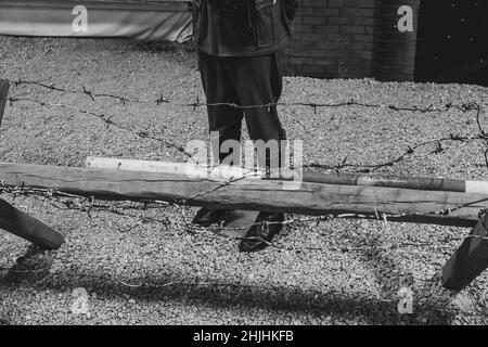 Ein Soldat in deutscher Uniform steht während des Zweiten Weltkriegs hinter einem Stacheldrahtzaun. Schwarzweiß-Foto. Stockfoto