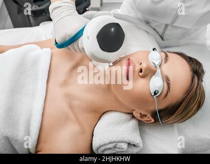 Fotorejuvenation des Gesichts einer Frau mit intensiv gepulster Lichtintensität IPL mit einer Kosmetikerin in einem Kosmetiksalon für die Rosazea-Behandlung, wobei braune Flecken entfernt werden Stockfoto