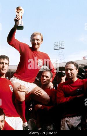 1966: Aktenfoto vom 1966. Juli von Englands Kapitän Bobby Moore, der von anderen Teammitgliedern getragen wird, als er die WM-Trophäe nach dem Sieg gegen Westdeutschland im Finale 4-2 in Wembley in London aushält. Ausgabedatum: Sonntag, 30. Januar 2022. Stockfoto