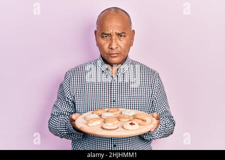 lateinischer Mann mittleren Alters hält Tablett mit Keksen deprimiert und sorgen für Not, weinen wütend und Angst. Trauriger Ausdruck. Stockfoto