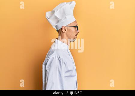 Glatze Mann mit Bart tragen professionelle Koch Uniform suchen zur Seite, entspannen Profil Pose mit natürlichen Gesicht mit selbstbewussten Lächeln. Stockfoto