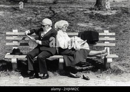 Ein älteres Paar, das sich auf einer Bank zurücklehnen und die New York Times lesen konnte. In Prospect Park, Brooklyn, New York. Ca. 1975. Stockfoto