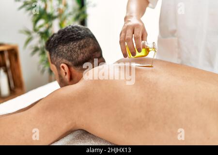 Junger hispanischer Mann mit Rückenmassage mit Öl im Beauty-Center Stockfoto