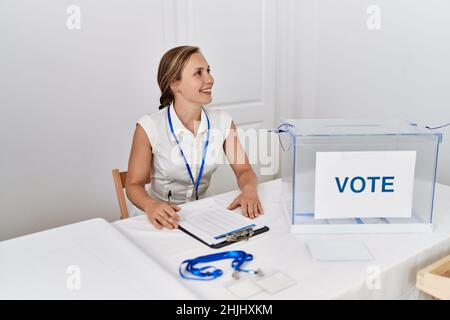 Junge kaukasische Frau lächelt selbstbewusst und schreibt auf der Zwischenablage, die an der Wahlhochschule arbeitet Stockfoto