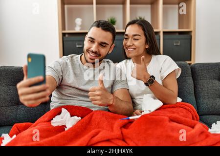 Junges lateinamerikanisches krankes Paar, das zu Hause eine medizinische Fernsultation mit dem Smartphone hat. Stockfoto