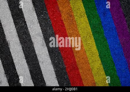 Regenbogenfarbene LGBT-Stolzflagge neben weißen Linien auf Asphalt, Draufsicht. Texturierter Hintergrund von bunt gestreiften Asphalt Hintergrund. Stockfoto