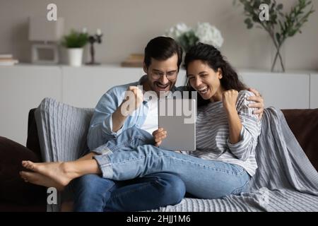 Paar lesen Nachrichten auf digitalem Tisch fühlen sich überglücklich Erfolg feiern Stockfoto