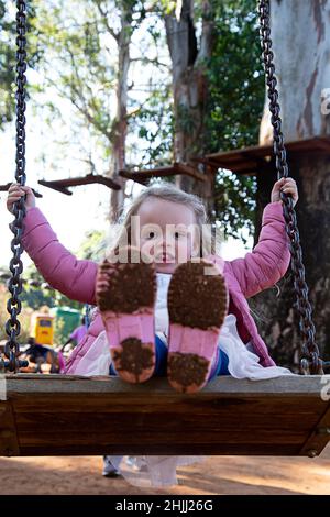 Junges Mädchen auf einer Schaukel in einem Park mit schlammigen gummistiefeln. Stockfoto