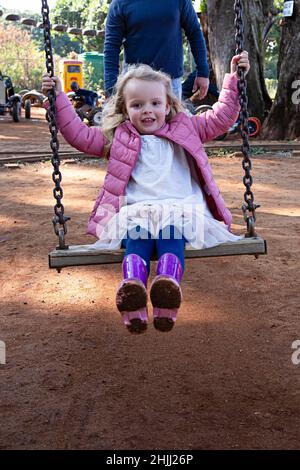 Junges Mädchen auf einer Schaukel in einem Park mit schlammigen gummistiefeln. Stockfoto