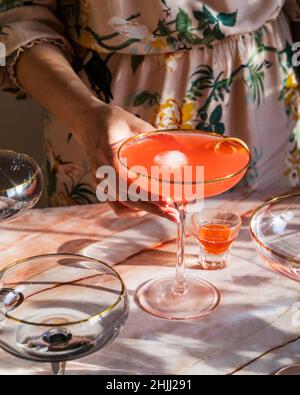 Mädchen hält Sommer Rhabarber Erdbeer Spritz Cocktail auf rosa Marmor Hintergrund. Mädchen Party Drink Ideen. Ideen für Brunch-Cocktails. Vertikale Aufnahme. Wählen Sie Stockfoto