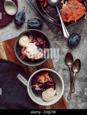 Pflaumenpflaster mit Vanilleeis auf einem Holzbrett auf grauem Steingrund. Draufsicht. Flaches Lay. Sommerfrüchte Dessert Stockfoto