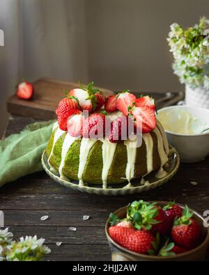 Grüner Spinat Kuchen mit Erdbeere auf einem dunklen rustikalen Holzhintergrund. Mädchen in weißem Kleid Gießen Sahnehäubchen auf Kuchen. Frühling Stillleben Stockfoto