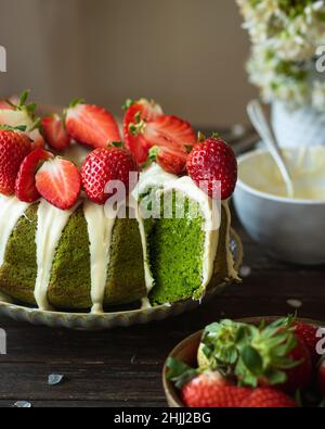 Grüner Spinat Kuchen mit Erdbeere auf einem dunklen rustikalen Holzhintergrund. Mädchen in weißem Kleid Gießen Sahnehäubchen auf Kuchen. Frühling Stillleben Stockfoto