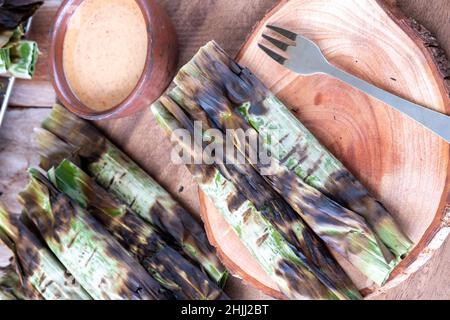 Gegrillter Fischkuchen aus gemahlenem Makrelenfisch, gemischt mit Gewürzen, dann in Bananenblätter gewickelt, über Holzkohle gegrillt, mit Erdnusssoße gegessen Stockfoto