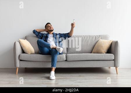 Junger arabischer Mann, der zu Hause die Klimaanlage anschaltet Stockfoto