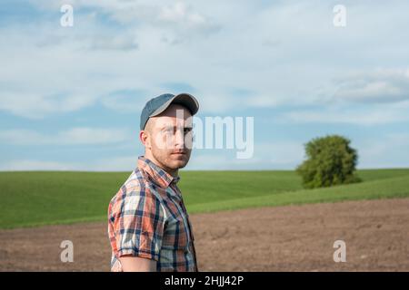 Porträt eines männlichen Agronomen, der Weizenfrüchte auf einem landwirtschaftlichen Feld inspiziert. Landwirt in einem Weizenfeld. Beurteilung der Getreideerträge Stockfoto