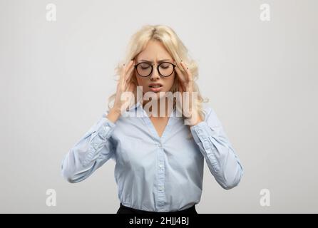Junge, müde Unternehmerin, die unter Kopfschmerzen und anrührenden Tempeln leidet und auf hellem Studiohintergrund steht Stockfoto