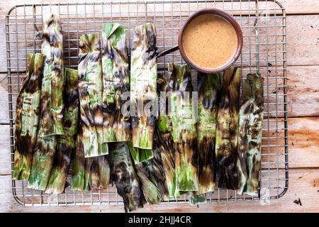 Gegrillter Fischkuchen aus gemahlenem Makrelenfisch, gemischt mit Gewürzen, dann in Bananenblätter gewickelt, über Holzkohle gegrillt, mit Erdnusssoße gegessen Stockfoto