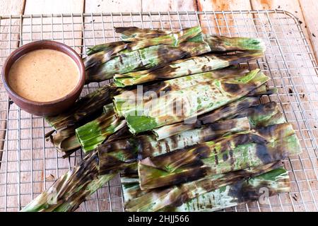 Gegrillter Fischkuchen aus gemahlenem Makrelenfisch, gemischt mit Gewürzen, dann in Bananenblätter gewickelt, über Holzkohle gegrillt, mit Erdnusssoße gegessen Stockfoto