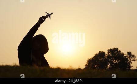 Glücklicher kleiner Junge mit einem Spielzeugflugzeug auf einem Sonnenuntergangshintergrund über einem Weizenfeld Stockfoto