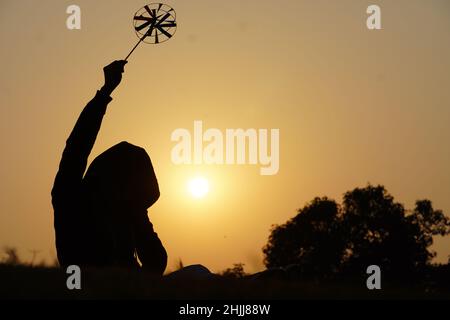 Fröhlicher kleiner Junge mit einem Spielzeug-Blütenblatt auf einem Hintergrund bei Sonnenuntergang über einem Weizenfeld Stockfoto