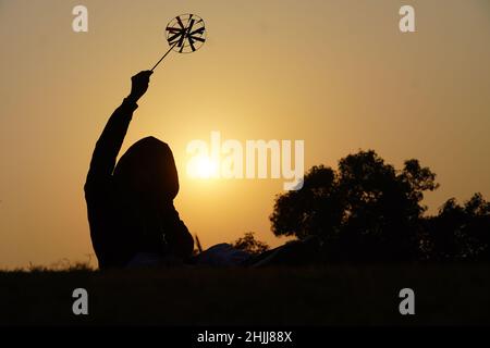 Fröhlicher kleiner Junge mit einem Spielzeug-Blütenblatt auf einem Hintergrund bei Sonnenuntergang über einem Weizenfeld Stockfoto