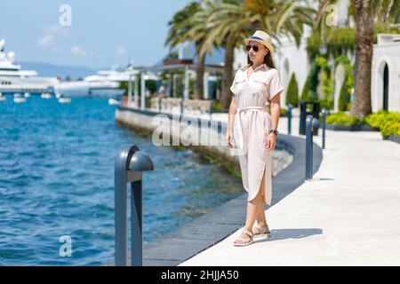 Junge Dame in Kleid und Hut beim Spaziergang in der Nähe des Hafenpiers Stockfoto
