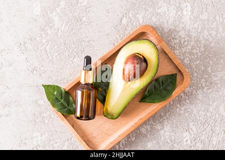 Molke- oder kosmetisches Avocado-Öl in einer Kosmetikflasche auf einem Holztablett mit reifer Avocado. Naturkosmetik Stockfoto