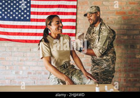 Fröhliche Militärangehörende, die im Militärkrankenhaus eine Dosis des Covid-19-Impfstoffs erhielt. Amerikanische Soldatin lacht glücklich, während sie sich injizieren lassen Stockfoto