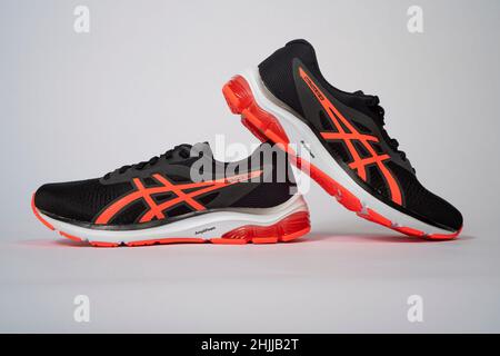 Ein Paar schwarze und orangefarbene Asics GEL-Pulse12 Laufschuhe, die isoliert auf weißem Hintergrund ausgeschnitten sind Stockfoto