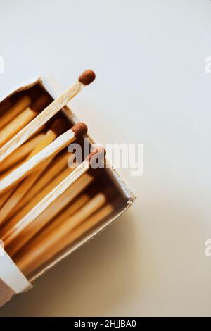 Auf einem weißen Tisch steht ein offener Karton mit Streichhölzern, aus dem drei Stücke herausragen. Haushaltsartikel. Brennbare Gegenstände Stockfoto