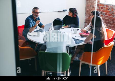 Eine Gruppe kreativer Geschäftsleute, die an einem modernen Arbeitsplatz ein Meeting abhalten. Ein erfahrener Geschäftsmann unterhielt seine Kollegen in einem Offi mit positiven Neuigkeiten Stockfoto